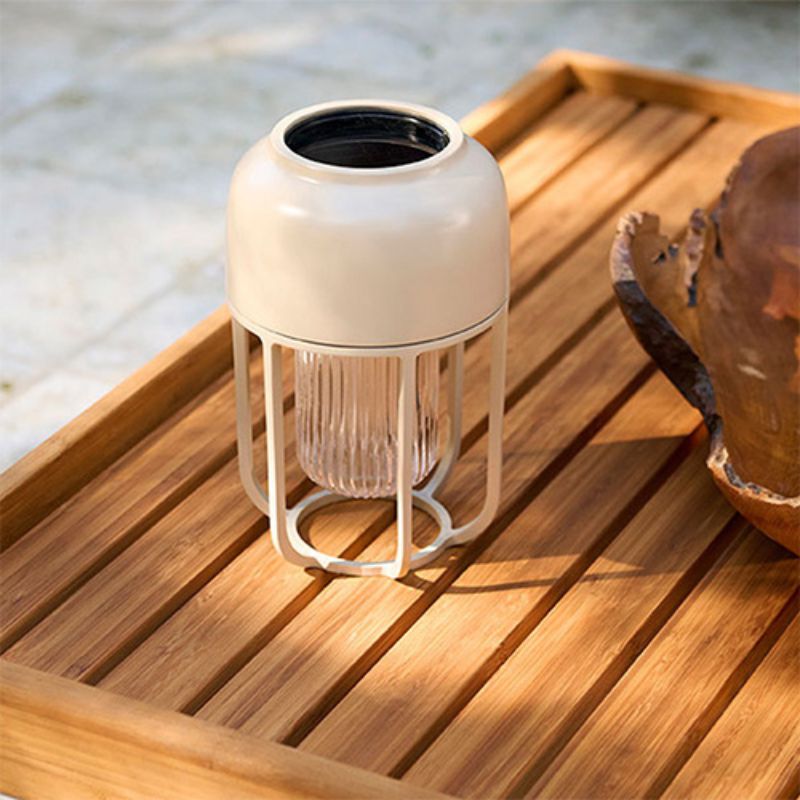 Cremeweiße solarbetriebene Tischleuchte für den Außenbereich mit mattem Metallgehäuse und Glasdiffusor, dekorativ platziert auf einem Holztablett im Garten